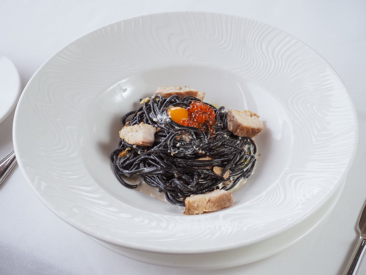 Elegant squid ink spaghetti garnished with salmon chunks and caviar on a stylish white plate.