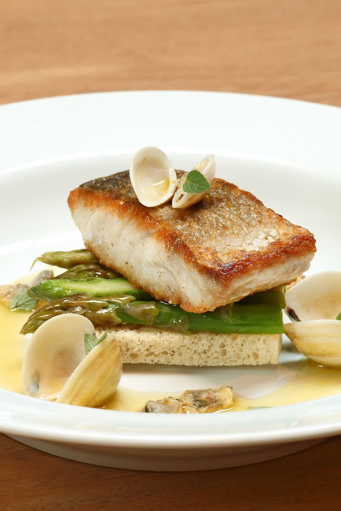A delectable fish filet served with asparagus and clams, elegantly plated.