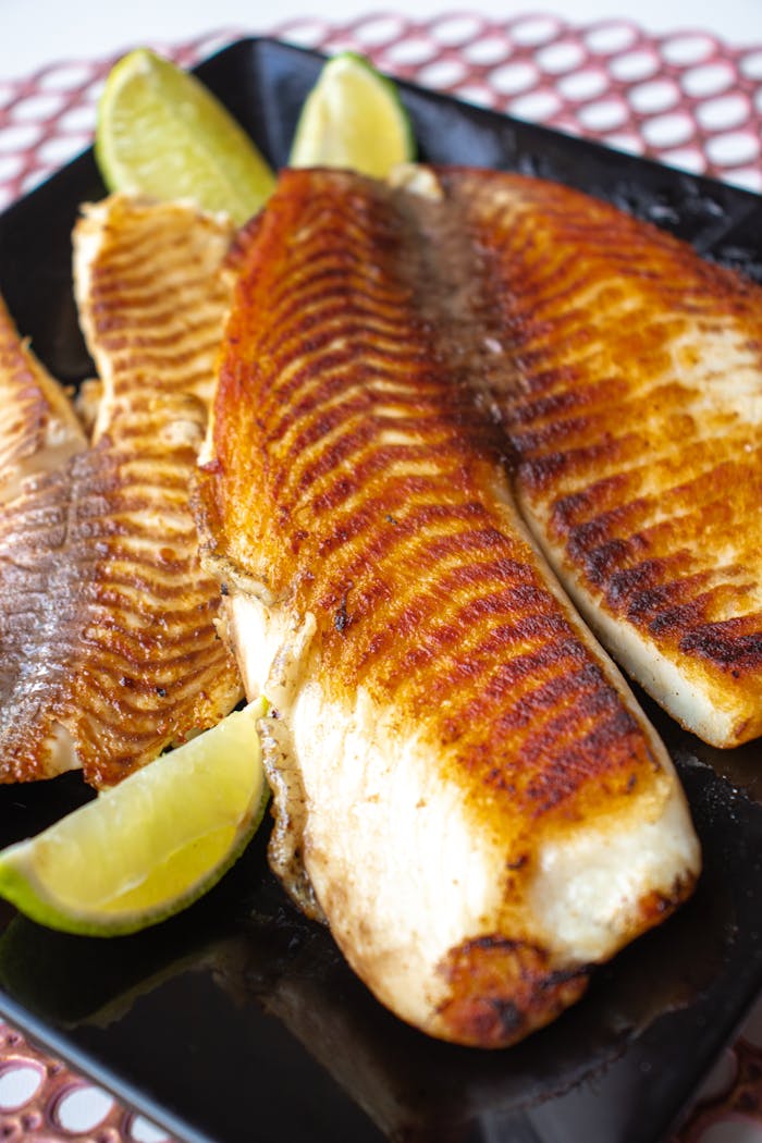 Deliciously grilled tilapia fillets served with lime wedges on a black plate.